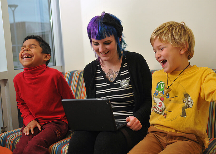 Student looking at a laptop with two laughing preschool kids